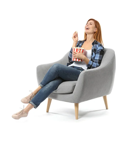 Beautiful woman with popcorn watching TV while sitting in armchair against white background — 스톡 사진