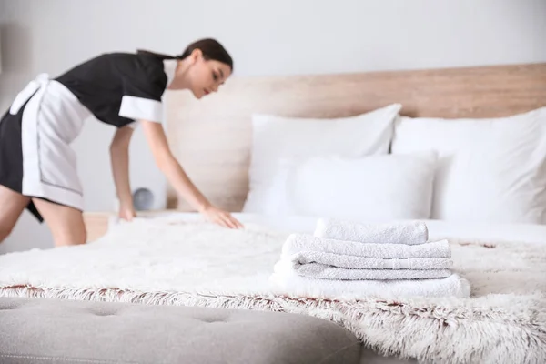 Linda camareira fazendo cama no quarto do hotel, foco em toalhas — Fotografia de Stock
