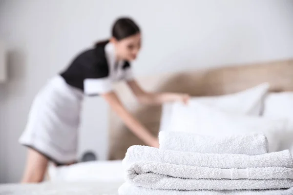 Beautiful chambermaid making bed in hotel room, focus on towels — Stock Photo, Image