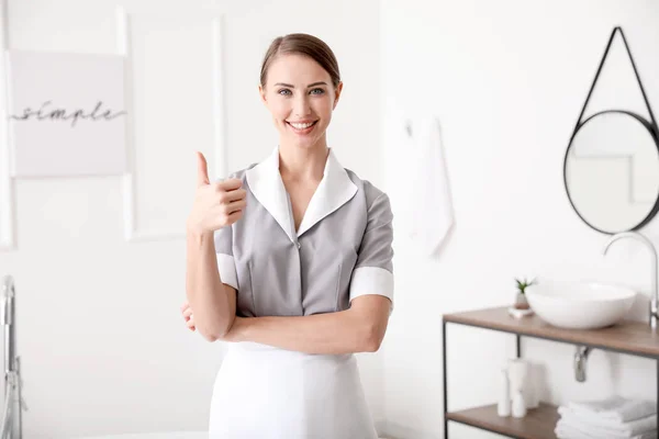 Beautiful chambermaid showing thumb-up in hotel bathroom — Stock Photo, Image