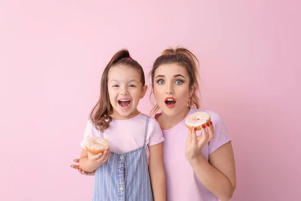 Sorpresa giovane donna e bambina con ciambelle su sfondo di colore — Foto Stock