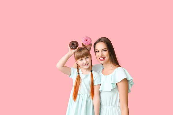 Beautiful young woman and little girl with donuts on color background — Stock Photo, Image