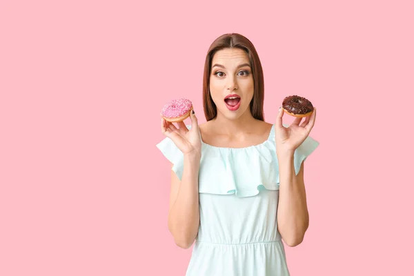 Beautiful surprised young woman with donuts on color background — Stock Photo, Image