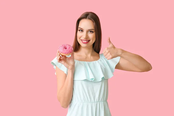 Beautiful young woman with donut showing thumb-up on color background — Stock Photo, Image