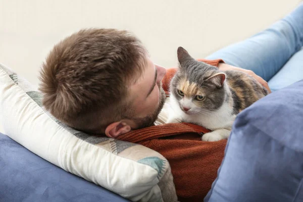 Man with cute cat lying on sofa at home — Stock Photo, Image