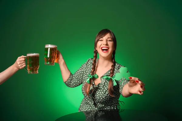 Funny young woman with beer at table against color background. St. Patrick\'s Day celebration