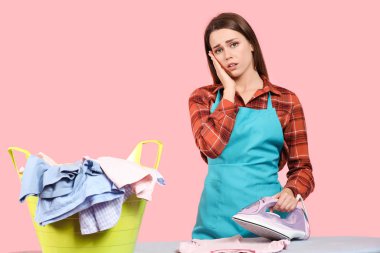 Çamaşır ve ütüden arkaplanı olan yorgun bir ev hanımı.