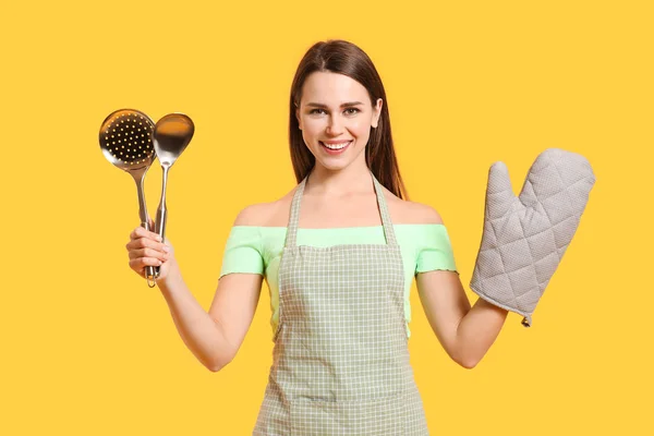 Joven ama de casa con utensilios de cocina sobre fondo de color —  Fotos de Stock