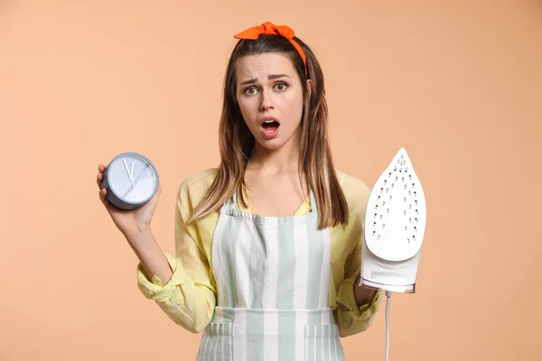 Stressed young housewife with iron and alarm clock on color background — 스톡 사진