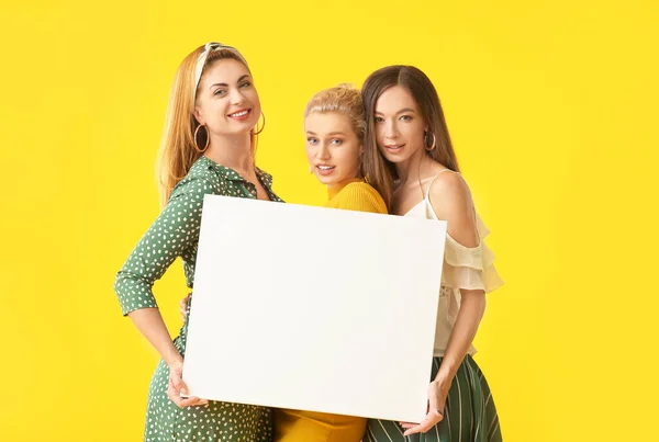 Hermosas mujeres jóvenes con póster en blanco sobre fondo de color — Foto de Stock