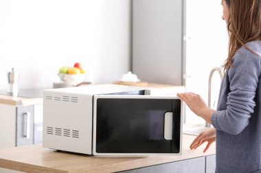 Woman opening modern microwave oven in kitchen