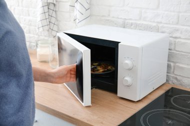 Woman opening modern microwave oven in kitchen