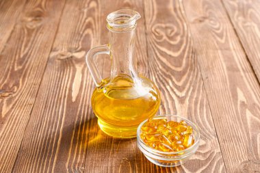 Jug of fish oil and capsules on wooden background