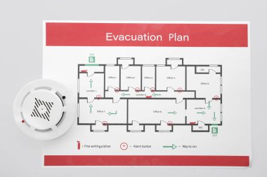 Evacuation plan and smoke detector on white background
