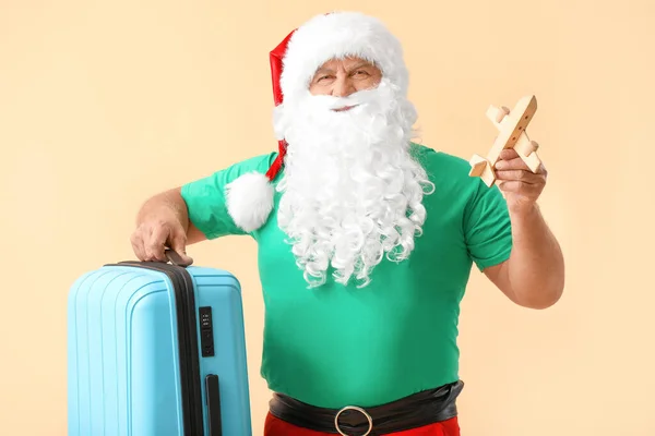 Санта Клаус з багажем і іграшковим літаком на кольоровому тлі. Концепція відпустки — стокове фото