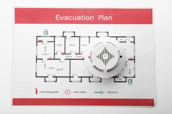 Evacuation plan and smoke detector on white background — ストック写真