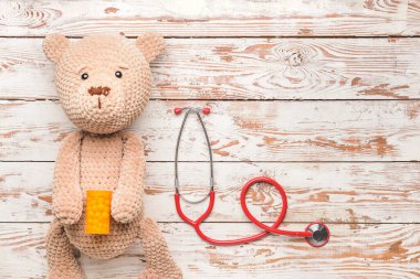 Stethoscope, pills and baby toy on wooden background