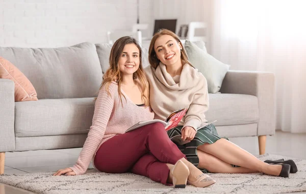 Young women in warm sweaters reading magazines at home — Stock Photo, Image