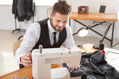 Atölyede dikiş makinesi üzerinde çalışan genç bir terzi.