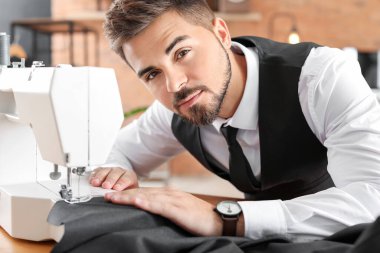 Atölyede dikiş makinesi üzerinde çalışan genç bir terzi.