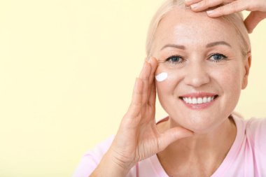 Güzel, olgun bir kadın yüz kremi sürüyor.