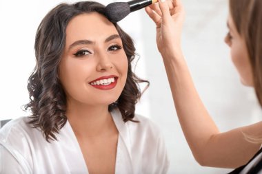Makyaj sanatçısı kuaförde genç ve güzel bir kadınla çalışıyor.