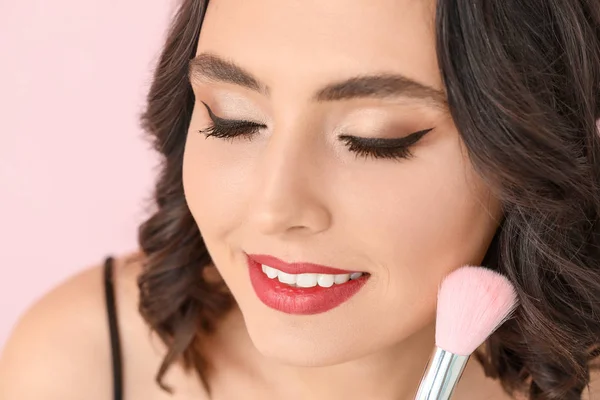 Bella giovane donna con trucco elegante e pennello su sfondo di colore, primo piano — Foto Stock