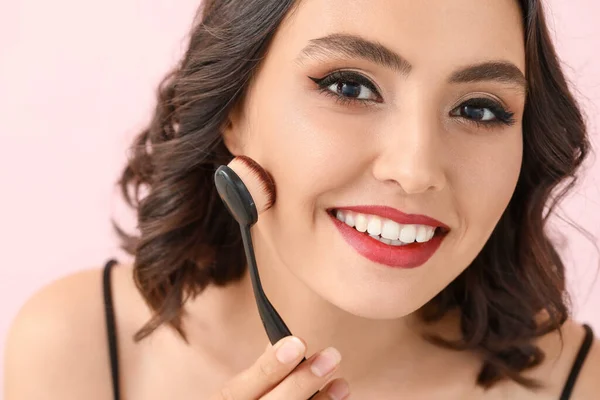 Beautiful young woman with stylish makeup and brush on color background — 스톡 사진