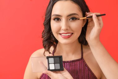 Renkli arka planda güzel genç bir kadınla çalışan bir makyöz.