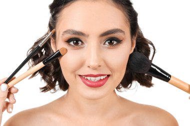 Şık makyajlı ve beyaz arka planda fırçaları olan güzel bir genç kadın.