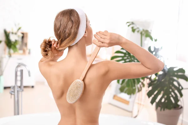 Beautiful young woman with massage brush in bathroom — Stock Photo, Image