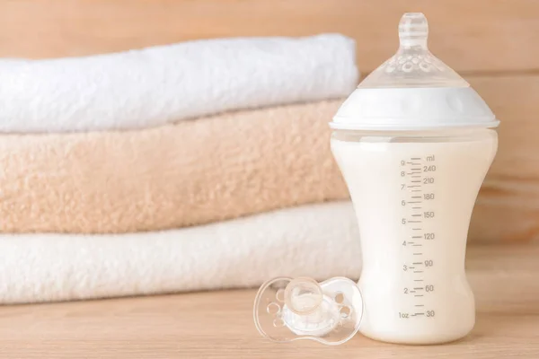 Bottle of milk for baby and pacifier on wooden table