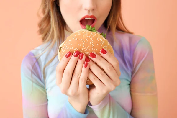 Junge Frau mit Burger auf farbigem Hintergrund, Nahaufnahme — Stockfoto