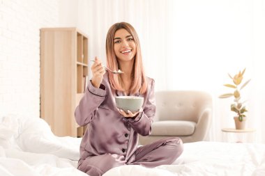 Güzel genç bir kadın yatakta kahvaltı yapıyor.