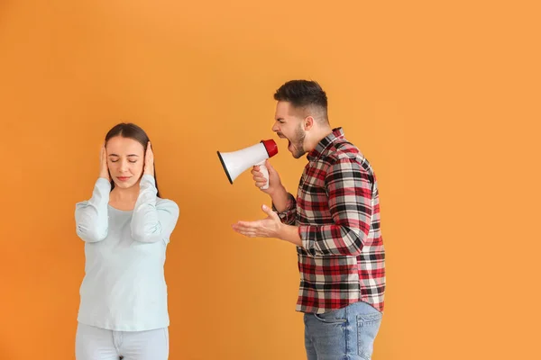 Angry man with megaphone shouting at his wife on color background — ストック写真