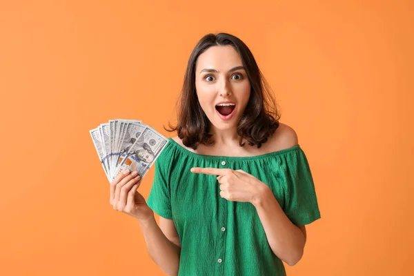 Surprised young woman with money on color background — Stock Photo, Image