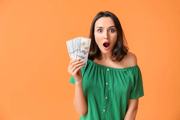Überraschte junge Frau mit Geld auf farbigem Hintergrund — Stockfoto
