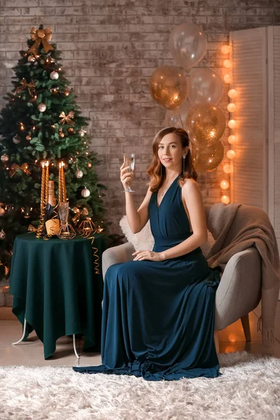Beautiful young woman with champagne in room decorated for Christmas — Stock Photo, Image