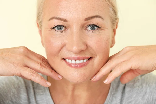 Mooie volwassen vrouw met gezonde huid op kleur achtergrond — Stockfoto