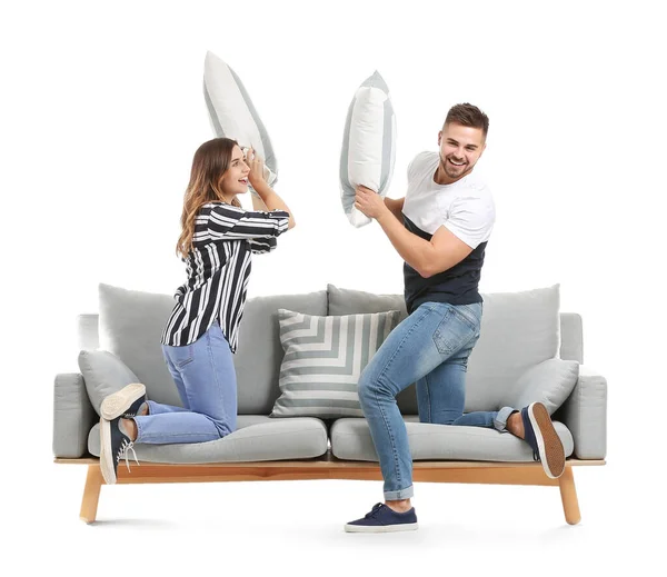 Young couple fighting pillows on sofa against white background — Stock Photo, Image