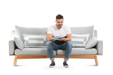 Genç adam beyaz arka planda kanepede otururken kitap okuyor.
