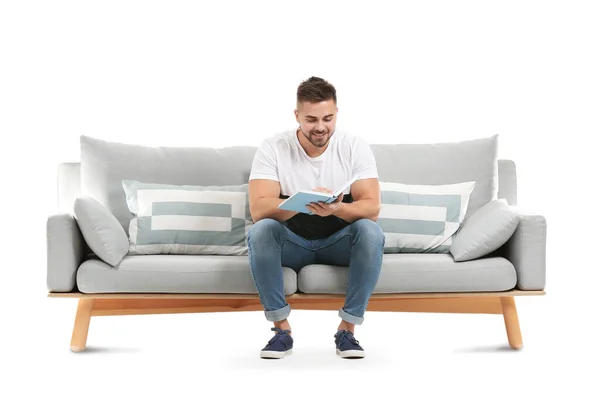 Jovem homem lendo livro enquanto sentado no sofá contra fundo branco — Fotografia de Stock