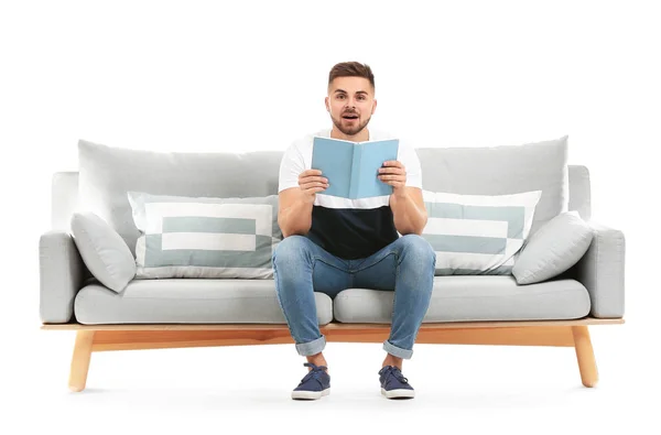 Young man reading book while sitting on sofa against white background — Stock Photo, Image