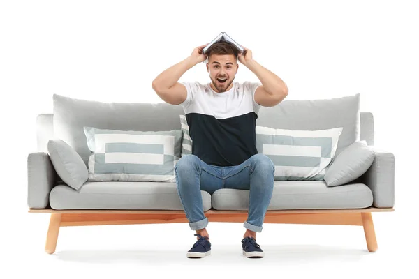 Young man with book sitting on sofa against white background — 스톡 사진