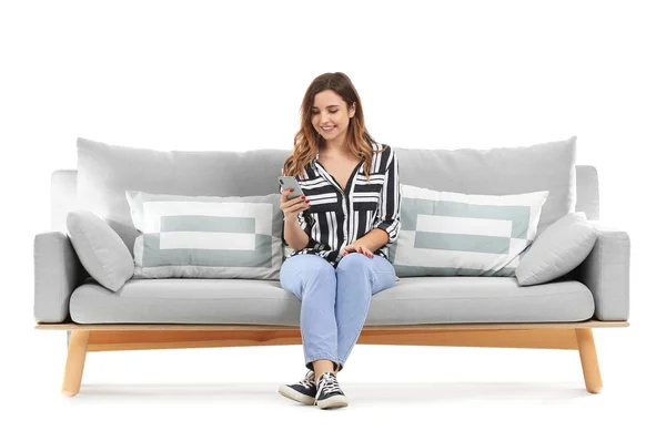 Fiatal nő mobiltelefon ül a kanapén, fehér háttér — Stock Fotó