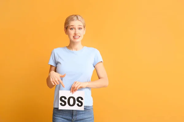 Mujer joven sosteniendo papel con la palabra SOS sobre fondo de color. Concepto de menstruación — Foto de Stock