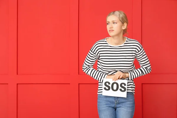 Mujer joven sosteniendo papel con la palabra SOS sobre fondo de color. Concepto de menstruación — Foto de Stock