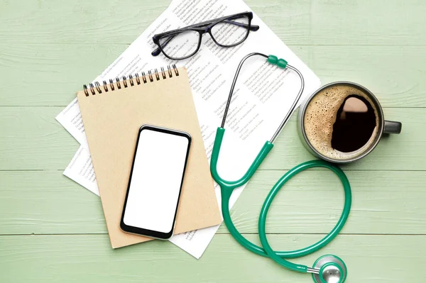 Stetoskop s mobilním telefonem, notebookem, dokumentem a šálkem kávy na stole — Stock fotografie