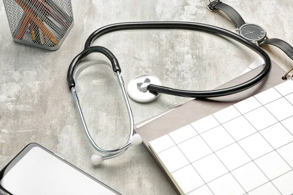 Stethoscope with stationery and mobile phone on grey background — Stock Photo, Image