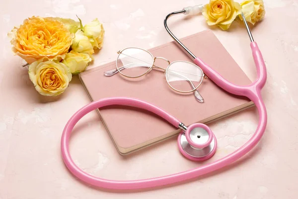 Stéthoscope avec fleurs, lunettes et cahier sur fond couleur — Photo